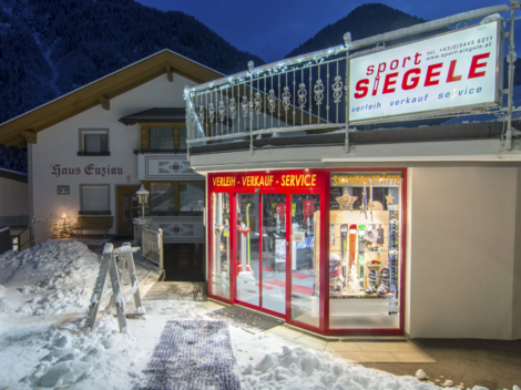 A sports store with large windows, located in a snowy environment at twilight. The building has a cozy atmosphere and is situated in the mountains.