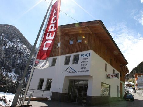 A modern shop with a wooden facade that offers ski rental and sales. The surroundings are mountainous and snow-covered.