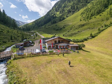 A picturesque landscape with an inn in the mountains. A river and green meadows surround the building.