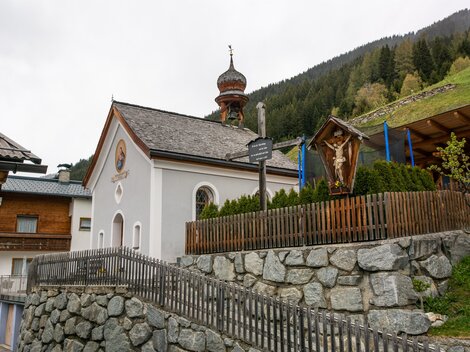 A small church with a distinctive dome and a lovely garden. In the background, green mountains can be seen. | © Bernhard Gruber – Photography