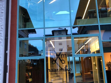 A modern hair salon with large glass windows. The name "naar.mike" is prominently visible on the door.